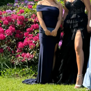 Mörkblå offshoulder klänning - Elegant mörkblå balklänning med offshoulder-design och hög slits. Perfekt för formella tillfällen.