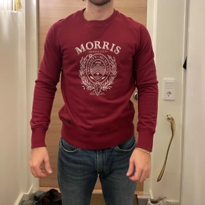 Vinröd tröja från Morris - Säljer en snygg vinröd tröja från Morris med tryck på framsidan. Tröjan har långa ärmar och en rund halsringning. Perfekt för en stilren look.