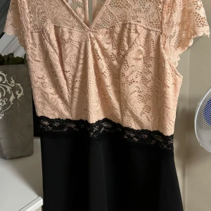 Rosa spetsklänning från Bodyflirt - Elegant klänning från Bodyflirt med en överdel i ljusrosa spets och en svart kjol. Klänningen har korta ärmar och en v-ringad design med spetsdetaljer. Perfekt för en stilfull look.