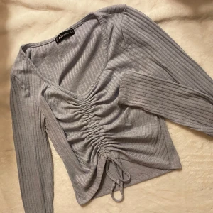 Grå ribbad tröja från Sister - Säljer en stilren grå ribbad tröja från Sister med v-ringning och snörning framtill. Tröjan har långa ärmar och en snygg, åtsittande passform. Perfekt för en trendig look!