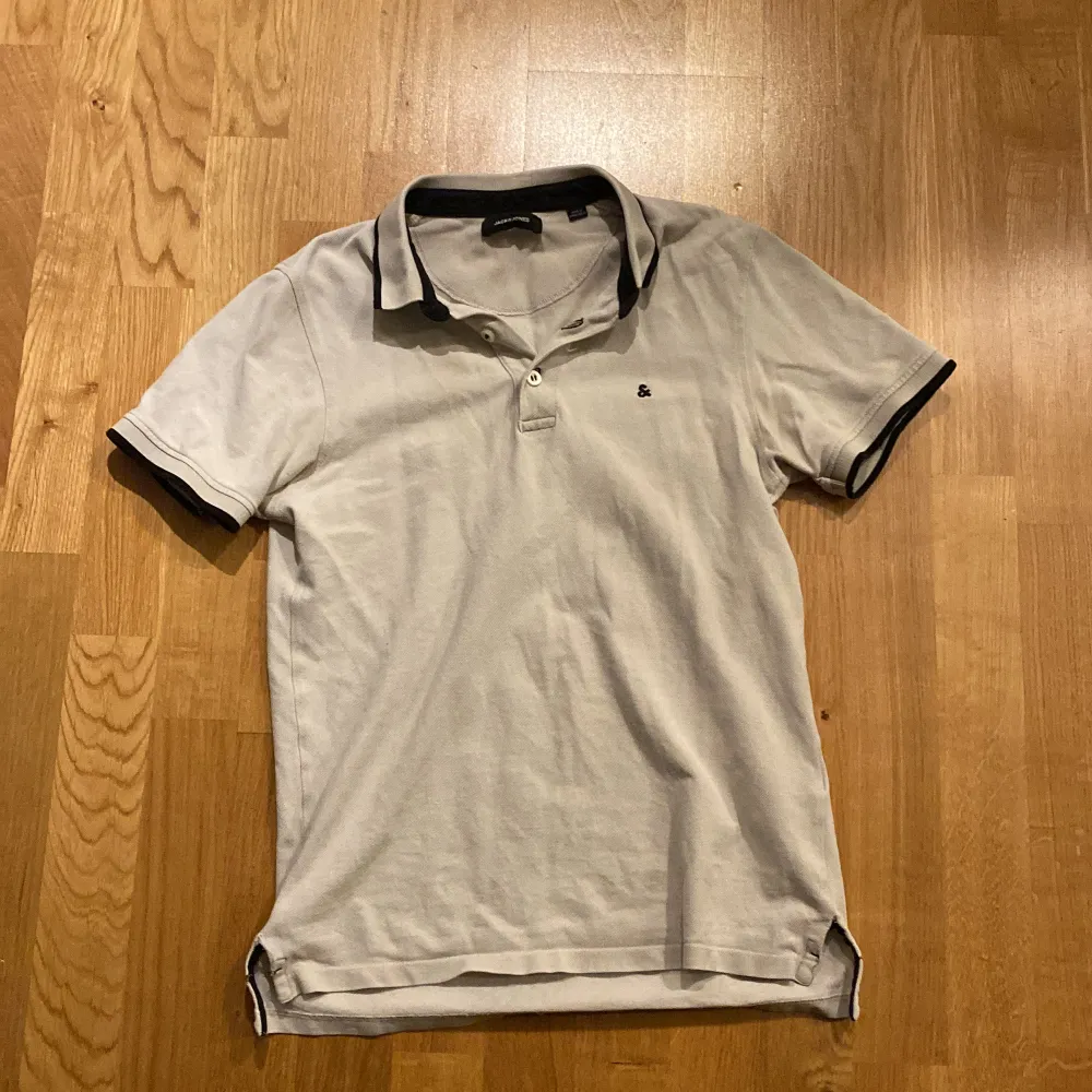 Snygg vit pikétröja från Jack & Jones med svart krage och ärmslut. Perfekt för en avslappnad stil. Tröjan har en klassisk passform och är kortärmad. Priset är absolut inte hugget i sten. T-paidat.