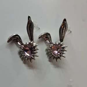 Silvriga örhängen med rosa stenar - Unika silvriga örhängen med en design som påminner om kaninöron. De har en vacker rosa sten i mitten som ger en glittrig effekt. Perfekta för att lägga till en lekfull touch till din stil. PRISET KAN DISKUTERAS