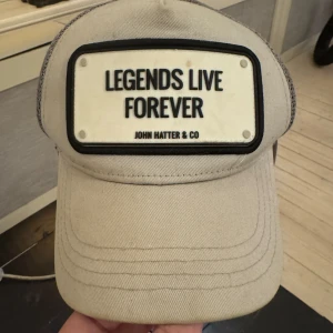 Grå keps från John Hatter & Co - Snygg grå keps med texten 'Legends Live Forever' på framsidan. Märket John Hatter & Co är broderat på insidan. Perfekt för en avslappnad stil.