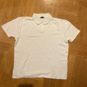 Vit pikétröja från Riley - Säljer en klassisk vit pikétröja från Riley i storlek M. Tröjan har korta ärmar och en stilren krage, perfekt för en avslappnad look. Köparen står så klart för frakt