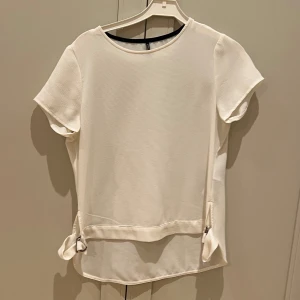 Vit blus med knytband - Elegant vit blus med korta ärmar och dekorativa knytband på. 