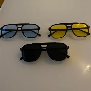 Tre par solglasögon med färgade linser - Säljer tre par solglasögon med olika färgade linser. Ett par med blå linser, ett med gula linser och ett med svarta linser. Alla har en klassisk rektangulär form och svarta bågar. Perfekta för att ge en cool touch till din stil.