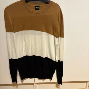 Randig tröja från Boss - Snygg tröja från Boss i brunt, vitt och svart. Den har ett randigt mönster och är långärmad med en rund halsringning. Perfekt för en stilren look.