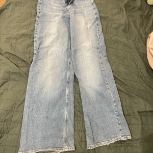 Blå jeansbyxor från CW - Säljer ett par snygga blå jeansbyxor från CW storlek 34. Byxorna har en hög midja och en bred passform som ger en avslappnad look. Perfekta för en trendig stil!