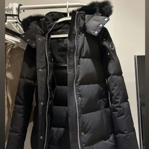 Svart dunjacka med pälskrage - Snygg svart jacka med pälskrage. Jackan har dragkedja och knappar framtill samt flera praktiska fickor. Perfekt för kalla vinterdagar.  Jackan är köpt förra året, den är som ny skick eftersom jackan endast använts ett fåtal gånger. Jackan är en tjej modell men passar till både kille och tjej alltså unisex. Den har storlek M men sitter även fint om man bär storlek S. Köpt från Johnells för 10 300 kr kvitto finns och säljs nu av mig för 5 900 kr. Hör av er vid intresse!