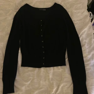 Svart kofta från Uniqlo - Säljer en stilren svart kofta från Uniqlo med knappar framtill. Den har långa ärmar och en klassisk passform som passar perfekt till olika outfits. Perfekt för lager-på-lager-stil!