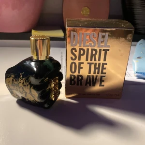 Diesel Spirit of the Brave Parfym - Diesel Spirit of the Brave är en parfym i en unik flaska formad som en knuten näve, med en elegant svart och guld design. Förpackningen är guldig med djärv text. Perfekt för den modige och självsäkre.