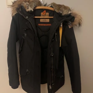Svart Parajumper jacka - Pris går att diskuteras!! Säljer en svart vinterjacka från Parajumpers med ÄKTA pälsfodrad huva och flera praktiska fickor. Jackan har dragkedja och knappar framtill samt en snygg patch på ärmen. Perfekt för kalla dagar och håller dig riktigt varm. Använd endast 1 vinterperiod. Priset går att diskuteras! Jag är 160cm lång och jackan hamnar precis under rumpan. Skicka gärna ett dm vid minsta intresse! Obs: det finns ett litet märke på framsidan men inget som syns tydligt vid använding.