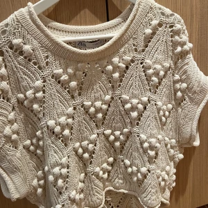 Beige stickad topp från Zara - Säljer en unik beige stickad topp från Zara med ett detaljerat mönster av trianglar och små bollar. Toppen har korta ärmar och en rund halsringning. Man kan styla den me nått under eller utan, supersnygg!