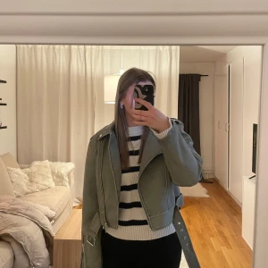 Khakifärgad skinnjacka med bälte - Snygg khakifärgad skinnjacka med dragkedja och  bälte. Prislapp kvar, nypris 489kr.