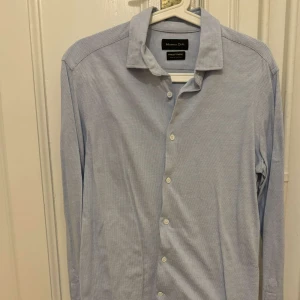 Blå skjorta från Massimo Dutti - Snygg blå skjorta från Massimo Dutti. Skjortan har långa ärmar och knappar framtill. Perfekt för en stilren look. Även stretch i materialet