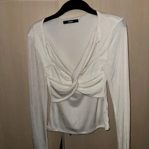 Vit långärmad topp från Bikbok - Elegant vit långärmad topp från Bikbok med draperad design framtill. Perfekt för en stilren look. Tillverkad i ett mjukt och bekvämt material.