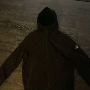 Svart jacka från Stone Island - Snygg svart jacka från Stone Island med huva och dragkedja. Tillverkad med Soft Shell-R e.dye® Technology för extra hållbarhet och flexibilitet. Perfekt för kyligare dagar.
