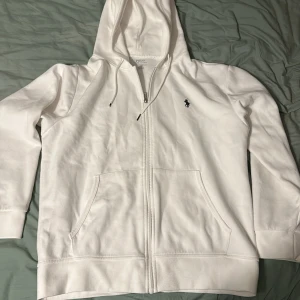 Vit hoodie från Polo Ralph Lauren - Säljer en stilren vit hoodie från Polo Ralph Lauren. Den har en dragkedja framtill och en klassisk broderad logga på bröstet. Perfekt för en avslappnad och snygg look. Öppen till byten som alltid och 10/10 skick på hoodien 