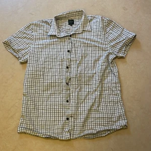 Rutig kortärmad skjorta från Blueprint - Säljer en snygg rutig skjorta från Blueprint i storlek L. Skjortan är kortärmad och har ett klassiskt rutmönster i svart och vitt. Perfekt för sommardagar eller avslappnade tillfällen. Den har knappar hela vägen ner och är i bra skick.