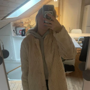 Beige kappa  - Stockholm lm kappa i beige, en knapp har gått av på ena sidan