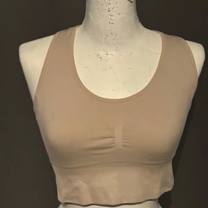 Beige sporttopp från Energetics - Säljer en superbekväm beige sporttopp från Energetics. Den är ärmlös och har en snygg korsad ryggdesign som ger extra stöd. Perfekt för träning eller yoga! Materialet är mjukt och stretchigt, vilket gör den idealisk för alla typer av rörelser.