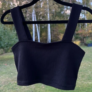 Svart crop top - En svart ribbad crop top från H&M. Toppen har breda axelband och ett mycket stretchigt material 🩷  Använd typ 2 gånger!  Storlek S 🌷  Längd: 18,5 cm Bandens bredd: 4 cm