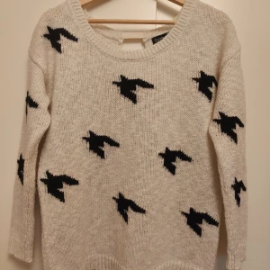 Beige stickad tröja med fågelmönster från Stradivarius - Säljer en superfin beige stickad tröja från Stradivarius med coola svarta fågelmönster. Tröjan har långa ärmar och en rund halsringning. Perfekt för höst och vinter! Notera att det finns en liten fläck på ena ärmen. Passar perfekt till jeans eller kjol för en avslappnad look.