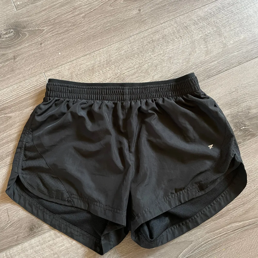 Säljer ett par svarta träningsshorts från Workout i storlek XS. De är gjorda i ett lätt och bekvämt polyester-material, perfekt för träning. Shortsen har en elastisk midja för en bra passform och en liten logga på sidan. Inga hål och inga fläckar.. Sportswear.