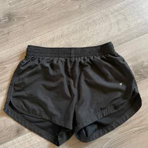 Säljer ett par svarta träningsshorts från Workout i storlek XS. De är gjorda i ett lätt och bekvämt polyester-material, perfekt för träning. Shortsen har en elastisk midja för en bra passform och en liten logga på sidan. Inga hål och inga fläckar.