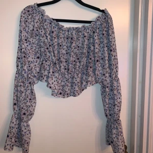 Blommig offshoulder topp - Säljer en superfin blommig offshoulder topp med volanger. Den har långa ärmar och är i en ljus färg med ett vackert blommönster i olika nyanser. Knappt använd så i väldigt fint skick 
