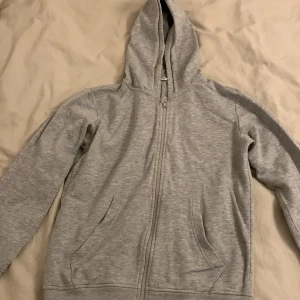 Grå huvtröja från Lindex - Säljer en grå huvtröja från Lindex i storlek 146/152. Den har en dragkedja framtill och två fickor. Perfekt för vardagsbruk och håller dig varm under kyliga dagar. Passar jättebra på mig som har xs! Tröjan är i bra skick och redo för en ny ägare!