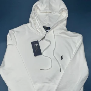 Polo Ralph Lauren Vit Hoodie *HELT NY + TAGS* - Ny och oanvänd Polo Ralph Lauren hoodie till salu! Denna klassiska hoodie kombinerar stil och komfort med en ikonisk logotyp. Perfekt för både vardag och sportiga aktiviteter. Missa inte chansen att lägga till detta tidlösa plagg i din garderob!