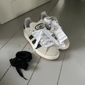 Adidas Campus sneakers i beige och svart - Säljer ett par snygga Adidas Campus sneakers i färgen crystal white. Helt nya med prislappen kvar tyvärr va de en  storlek för små för mig. Nypris 1350. Släpper de för första rimliga bud!!