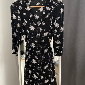 Svart blommig klänning från Mango - Säljer en superfin svart klänning från Mango med vita blommor. Den har trekvartsärmar och knappar framtill, vilket ger en söt och casual look. Perfekt för både vår och sommar! 🌸