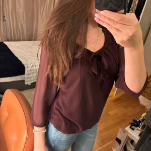 Vinröd blus med knytband - Säljer en elegant vinröd blus med knytband vid halsen. Blusen har trekvartsärmar och är perfekt för både vardag och fest. Materialet är lätt och luftigt, vilket gör den bekväm att bära hela dagen.