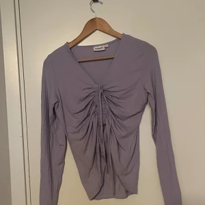 Ljuslila långärmad topp från kapphal  - Säljer en superfin ljuslila topp från Monki. Känns lite stor i storleken. Den har en snygg v-ringning och coola rynkdetaljer framtill som ger en unik look. Perfekt för både vardag och fest! 💜