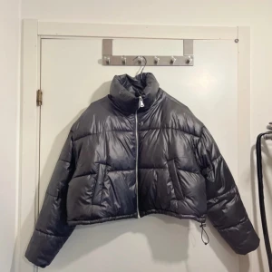 Svart pufferjacka - Säljer en snygg svart glansig pufferjacka i croppad modell. Jackan har en dragkedja framtill och långa ärmar.