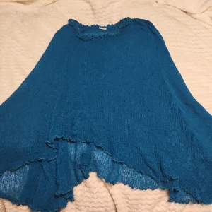 Blå poncho från Ulla Jacobsson - Säljer en härlig turkos poncho från Ulla Jacobsson. Den har en lös passform med volangdetaljer längs kanterna. Perfekt för alla tillfällen! 💙