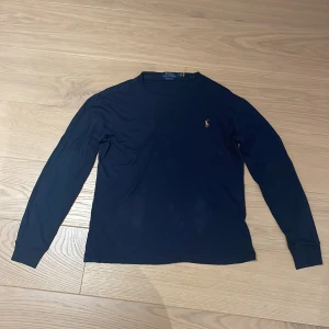 Mörkblå långärmad t-shirt från Polo Ralph Lauren | köpt för 800 kr - Säljer en snygg mörkblå långärmad t-shirt från Polo Ralph Lauren i storlek S. Tröjan har en broderad logga på bröstet och är i slim fit. Perfekt för vardagen! T-shirten är köpt för 800 kr och är knappast använd.