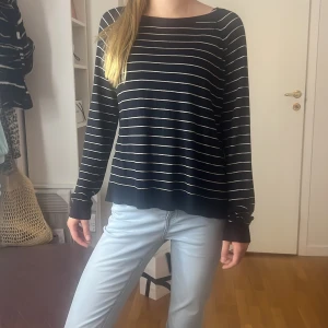 Svart och vit randig tröja - Säljer en snygg svart tröja med vita ränder. Den har en avslappnad passform och långa ärmar, perfekt för både vardag och lite kyligare dagar. Tröjan är supermjuk och bekväm att ha på sig. Passar perfekt till jeans för en casual look!