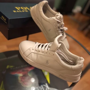 Vita sneakers från Polo Ralph Lauren - Säljer ett par snygga vit sneakers från Polo Ralph Lauren. De är i nyskick och har en stilren design med snörning. Perfekta för vardagarna. Obs, det är inte orginal sko lådan men den skickas med ändå!🙏🐎