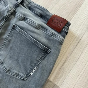 Grå jeans från Scotch & Soda - Säljer ett par snygga grå jeans från Scotch & Soda. De har en klassisk femficksdesign och en diskret tvättad look. Jeansen är i en slim passform och har en knappgylf. Perfekta för både vardag och fest! Nypris: 990kr