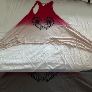 Rosa och beige ärmlös topp - Säljer en superfin slutsåld ärmlös H&M Coachella topp i rosa och beige med ett coolt svart mönster framtill. Perfekt för sommardagar eller festivaler! Den har en avslappnad passform och är gjord i ett mjukt material som känns skönt mot huden.