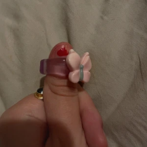 Lila ring med fjärilsdetalj - Superfin lila ring med en söt rosa fjäril på toppen. Ringen är i en genomskinlig lila nyans och fjärilen har en liten grön detalj i mitten. Perfekt för att lägga till en lekfull touch till din outfit! 🦋