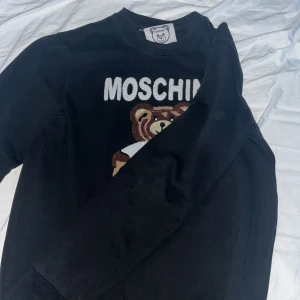 Moschino - Säljer en stilren Moschino-tröja med den ikoniska nallebjörnen. Jag har använt den 6-9 gånger, så den är i mycket bra skick. Perfekt för dig som vill ha något unikt och trendigt!  Storlek: M Pris: 1999kr  Hör