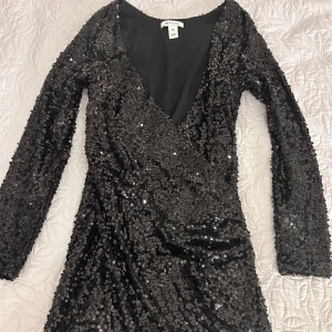 Svart paljettklänning från NLY One - Säljer en superglittrig svart klänning från NLY One i storlek XS. Den har en djup v-ringning och är täckt med paljetter som verkligen fångar ljuset. Perfekt för en fest eller nyårsafton! Klänningen har långa ärmar och en tight passform som ger en snygg siluett.