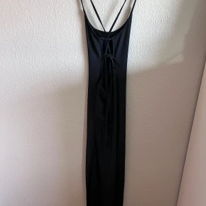 Svart långklänning med snörning - Säljer en elegant svart långklänning med smala axelband och en snygg snörning i ryggen. Perfekt för festliga tillfällen eller en utekväll. Klänningen har en tight passform som framhäver figuren.