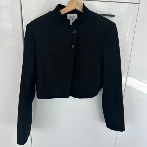Croppad blazer från Zara - Croppad blazer med vadderade axlar från Zara. Blazern har två stycken knappar framtill. Använd 1 gång, nypris 559 kr. 