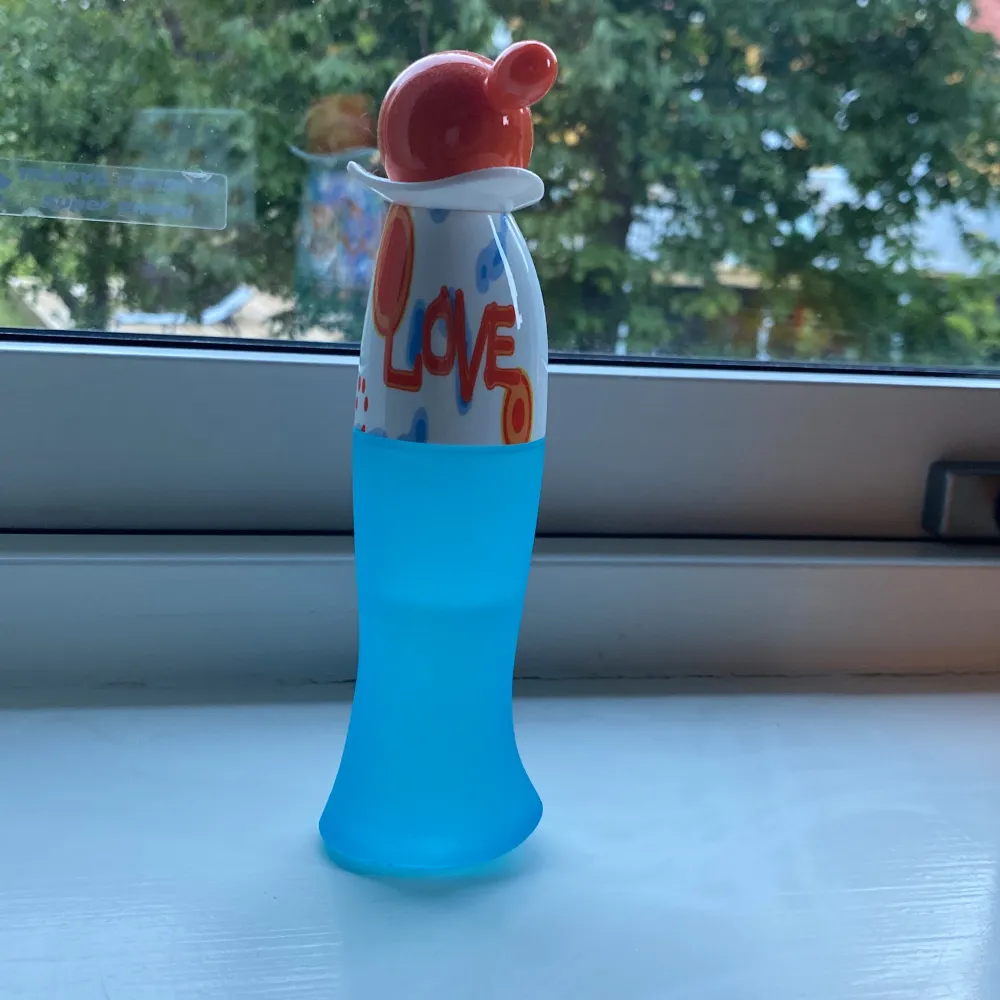 Säljer en superfin parfymflaska från Moschino, 'I Love Love'. Flaskan är i en cool blå färg med en unik form och har en rolig orange och vit kork. Den rymmer 50 ml, hälften har använts och är perfekt för att ge en fräsch och glad doft. Perfekt för dig som älskar färgglada och lekfulla design!. Parfym.