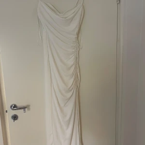 Vit klänning - Vit klänning med korsett och drapering över. Rynkning på sidan och slits 